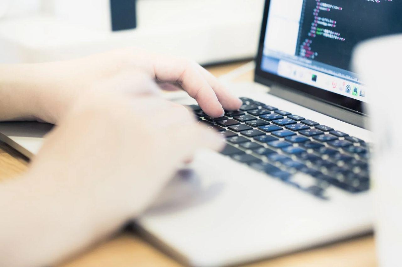 RubyとHaskellのロゴがスピードメーターを挟んで対峙し、背景にコードとコンパイラのアイコン